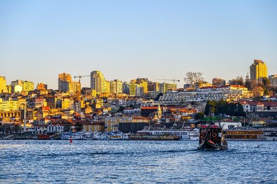 A tour boat moves on the Douro River during the dusk hours, with