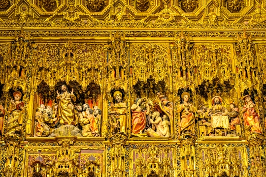 Low-angle view of the main altar featuring a group of statues of religious saints and a gold-colored surface.