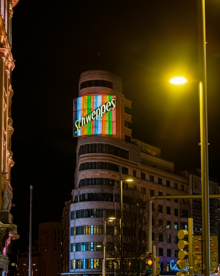 Night view of the illuminated sign for Schweppes on top of a bui