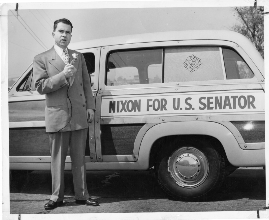 Richard Nixon stands in front of his campaign automobile and hol